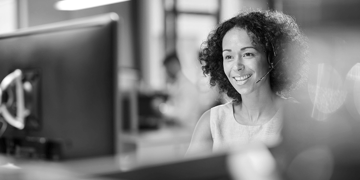 Smiling woman wearing a headset and sitting in front of a computer